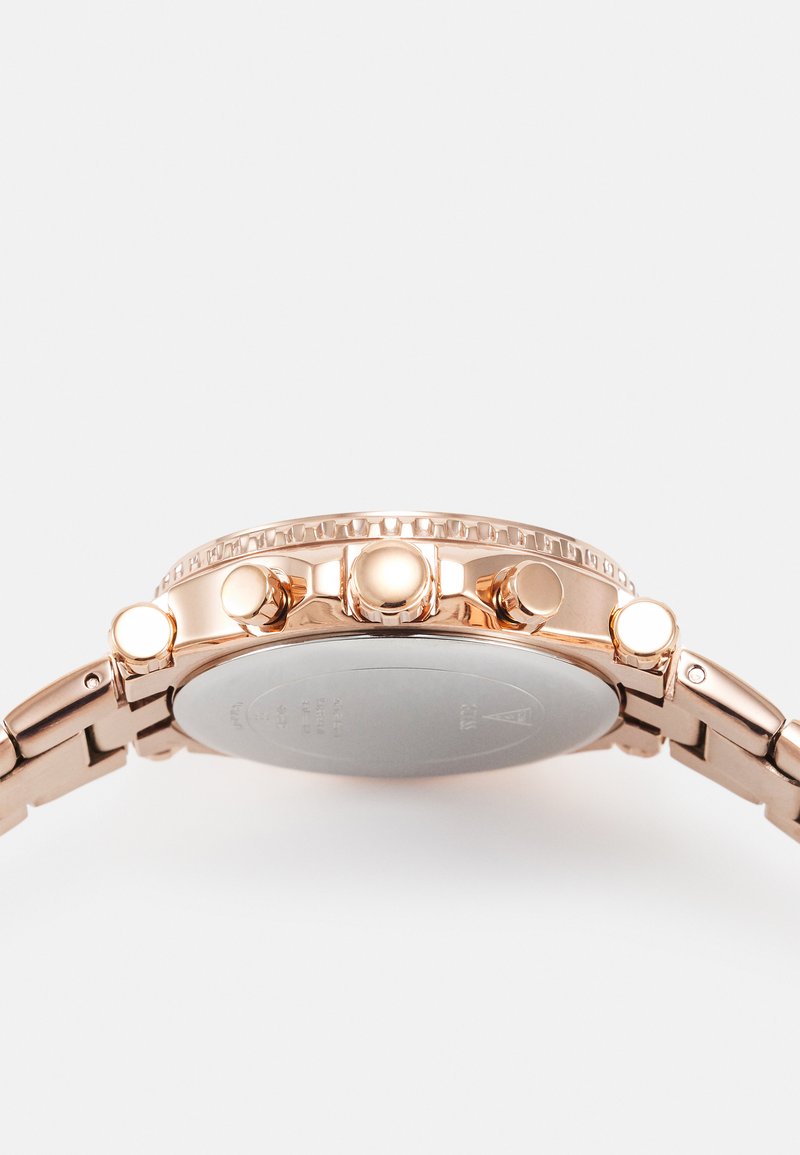 Montre en or rose avec un bracelet en acier inoxydable, lunette texturée, trois boutons-poussoirs et un fond de boîte argenté lisse.