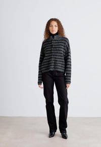 Gray and black striped cardigan with a high collar, button closure, and long sleeves, paired with black pants and pointed shoes.