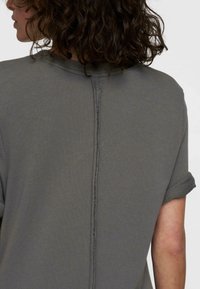 Haut en tricot gris avec de courtes manches roulées, présentant un détail de couture vertical au dos et un tissu texturé.