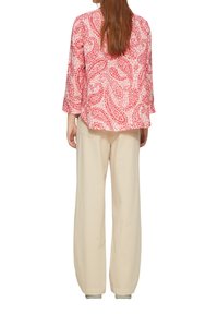 Rood en wit paisley-gepatteerde blouse met driekwartmouwen, gecombineerd met crèmekleurige wijde broek gemaakt van een lichtgewicht materiaal.