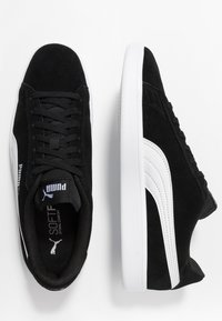 Black suede sneakers with white leather accents; flat laces, padded collar, and a rubber sole; features Puma logo on the tongue and side.