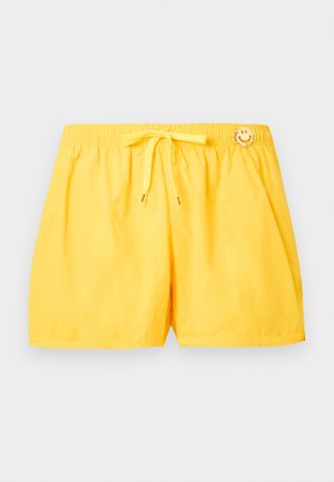 Shorts de bain jaune vif avec taille élastique, cordon de serrage et petite écusson smiley près de la taille sur un fond uni.