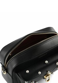 Borsa a tracolla in pelle nera con dettagli dorati, doppie cerniere, accenti di perle sulla parte anteriore e una fodera interna con marchio.