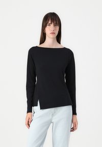 Black long-sleeve top with a boat neckline and side slits. Smooth cotton fabric, fitted design, and minimalistic look, paired with light jeans.