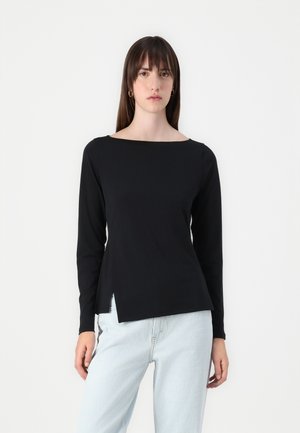 Top nero a maniche lunghe con scollatura a barca e spacchi laterali. Tessuto di cotone liscio, design aderente e look minimalista, abbinato a jeans chiari.