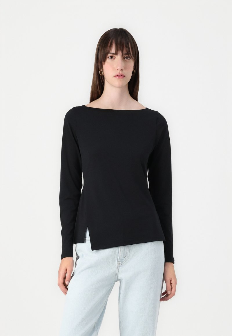 Black long-sleeve top with a boat neckline and side slits. Smooth cotton fabric, fitted design, and minimalistic look, paired with light jeans.