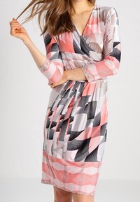 Sukienka kopertowa z geometrycznym wzorem w kolorze różowym, czarnym i białym. Wykonana z miękkiego, elastycznego materiału, z rękawami o długości trzy czwarte oraz zebranym w talii.
