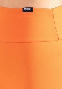 Oranje, rekbare stof met een gladde textuur, met een zwart label aan de taille met de merknaam "SMILOOX".