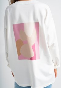 Felpa bianca con una grande grafica astratta nei toni di rosa pallido, beige e crema sul retro. Vestibilità ampia con scollatura a coste.