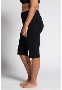 Leggings capri neri in cotone con vita elasticizzata, design a gamba affusolata e texture liscia, indossati da un modello di profilo.