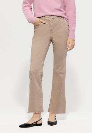 Beige flared jeans with a mid-rise waist, featuring a raw hem and five pockets, paired with black pointed flats and a pink sweater.