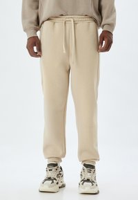 Pantalones deportivos beige hechos de un material suave, con una cintura elástica con cordón y puños ajustados en los tobillos.