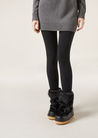 Czarne botki z sztucznego futra za kostkę z masywną podeszwą, charakteryzujące się gładkim skórzanym wykończeniem i dekoracyjnymi krzyżującymi się sznurówkami. Noszone z czarnymi legginsami i swetrem.