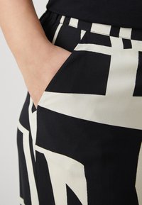 Tissu à motifs noir et crème montrant un gros plan d'une poche avec une coupe décontractée, une taille élastique et une texture lisse.