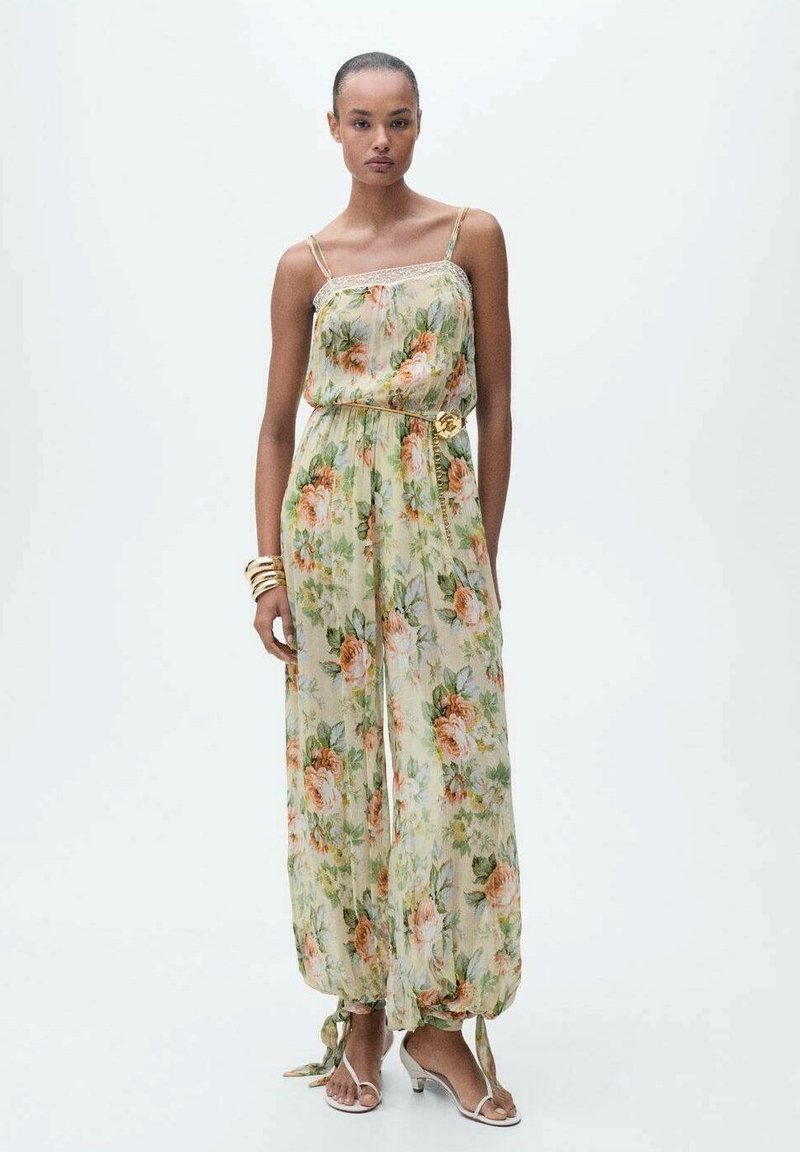 Floral jumpsuit in sheer fabric with a light green background, adorned with orange roses. Features adjustable straps and a belted waist.