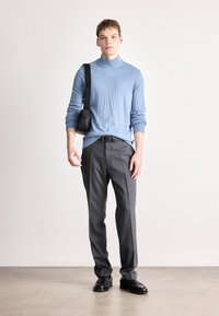 Ανοιχτό μπλε πλεκτό πουλόβερ με ψηλό λαιμό σε συνδυασμό με γκρι προσαρμοσμένα παντελόνια. Μαύρη τσάντα ώμου φορεμένη χιαστί. Μαύρα γυαλιστερά παπούτσια ολοκληρώνουν την εμφάνιση.