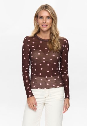 Braunes durchscheinendes Langarmoberteil mit großen pinken Pünktchen, rundem Ausschnitt und gewelltem Saum. Trägt man über hellfarbigen Hosen für einen Kontrast.