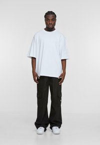 Hvid oversized t-shirt med korte ærmer, parret med løse sorte cargo bukser med flere lommer og knapdetaljer, båret med hvide sneakers.
