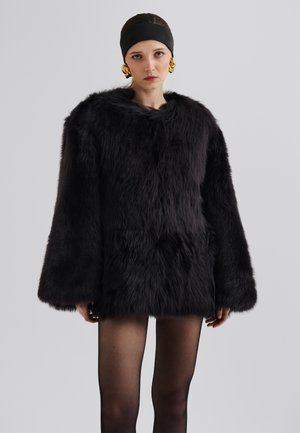 Veste en fausse fourrure noire avec des manches oversized et un col haut, présentant une surface texturée et pelucheuse ainsi qu'une coupe décontractée.