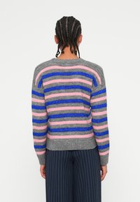 Grå genser med horisontale striper i rosa, blått og mørkegrått. Har rund hals og strukturert strikk. Kombinert med marineblå stripete bukser.