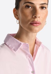 Pink collared shirt made of smooth fabric, featuring a subtle sheen and a single button at the collar. Simple, clean design with no patterns.