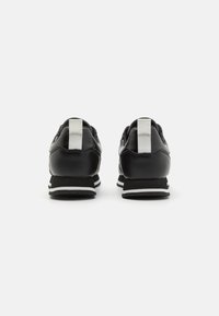Zapatos deportivos negros con una parte superior de cuero suave, acentos blancos y un talón acolchado. Cuenta con una lengüeta texturizada y una suela de goma a rayas.