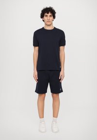 T-shirt de algodão azul-marinho com mangas curtas, combinado com calções até ao joelho coordenados. Apresenta detalhes de logo. Ténis brancos completam o visual.