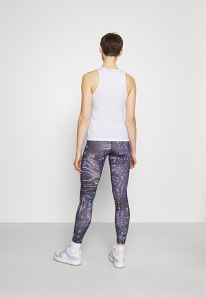 Weißes ärmelloses Oberteil mit hohem Ausschnitt, kombiniert mit bunten, gemusterten Leggings mit wirbelnden Designs in dunklen Tönen und Akzenten.
