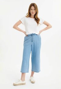 Biely kratučký rukávový top s krajkovým detailom, skombinovaný so svetlomodrými širokými denimgovými nohavicami s pásom na šnurovanie. Biely tenisky s juta podrážkou.