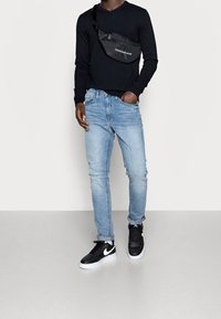 Svart långärmad tröja, ljusblå slitna skinny jeans och svarta Nike sneakers med vita sulor. Svart axelremsväska med logotyp.