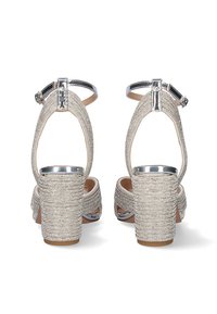 Sandalias plateadas de tacón con parte superior de tela trenzada, correa en el tobillo y tacón bloque grueso. Presenta acentos metálicos y un diseño de parte trasera abierta.