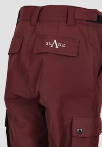 Pantaloni cargo color bordeaux con una texture liscia, dotati di tasche applicate e un logo sul retro. Include una vita regolabile e dettagli con bottoni a scatto.