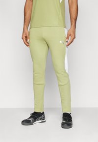 Pantalons de sport verts avec panneaux latéraux blancs, design ajusté, taille élastique et logo Puma. Portés avec des chaussures de sport noires.