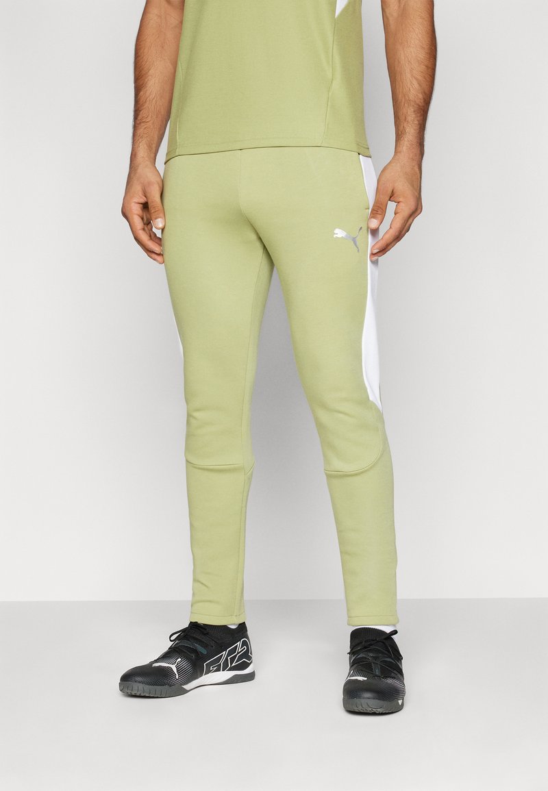 Pantalons de sport verts avec panneaux latéraux blancs, design ajusté, taille élastique et logo Puma. Portés avec des chaussures de sport noires.