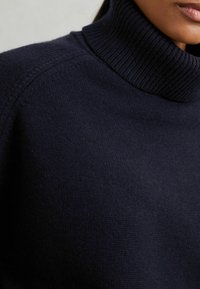 Pull col roulé bleu marine avec col côtelé. Fabriqué en tissu tricoté doux et texturé, avec des détails de couture subtils sur l'épaule.