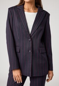 Blazer a righe navy con linee fucsia. Design sartoriale, due bottoni, rever a punta e tasche laterali. Texture del tessuto liscia.