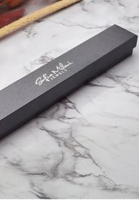 Scatola per gioielli rettangolare nera con texture e logo in rilievo "Sofia Milani Jewels" sul coperchio, appoggiata su una superficie di marmo.