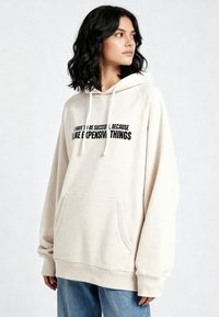 Felpa con cappuccio color crema realizzata in tessuto morbido, con tasca a marsupio e stampa nera. Maniche lunghe e vestibilità comoda con polsini a costine.