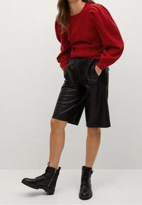 Pull en tricot rouge avec des manches bouffantes, assorti à un bermuda en simili cuir noir et des bottines noires à lacets.