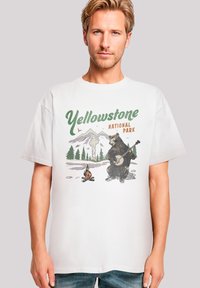 White cotton T-shirt featuring a graphic of a bear playing a banjo in a natural setting, with "Yellowstone National Park" text in green and orange.