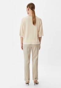 Jasno beżowa, luźna bluzka z szerokimi rękawami, warstwowy fason. Zestawiona z jasnymi spodniami i lekkimi butami na obcasie, utrzymana w jednolitej kolorystyce.