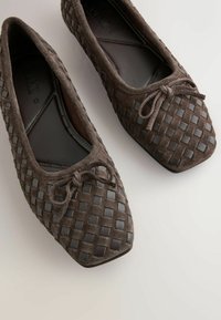 Barna szarvasbőr balerina cipő fonott részletekkel és szögletes orral. Elől díszes masni, belül pedig sima bélés található.