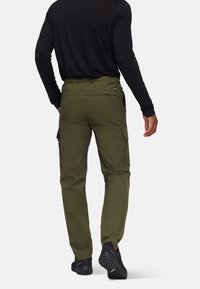 Olijfgroene cargobroek met zijzakken, elastische tailleband en een taps toelopend ontwerp, gecombineerd met een zwart langetermijn top en zwarte schoenen.