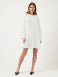 Robe blanche à manches longues, texturée avec un tissu à volants superposés, longueur au-dessus du genou, ourlet brut, associée à des chaussures noires à bout pointu.