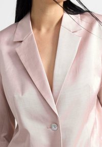Blazer rosa chiaro realizzato in tessuto testurizzato con rever a scudo e chiusura a un bottone, che mette in risalto una vestibilità sartoriale e una finitura liscia.