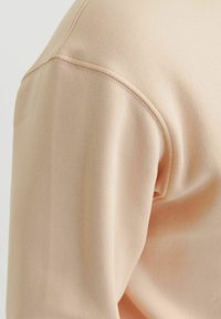 Licht perzikkleurige sweatshirt met een soepel materiaal, ronde schoudernaden en ribgebreide accenten op de manchetten en de halslijn. Subtiele textuur zichtbaar.