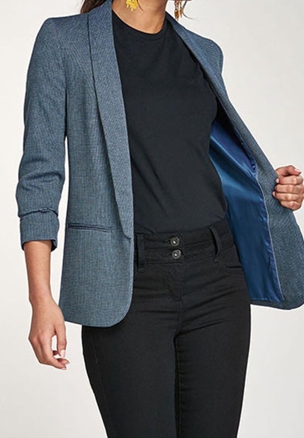 Femme portant un blazer bleu aux manches retroussées sur un haut noir et un pantalon noir taille haute, tenant le blazer ouvert pour montrer la doublure en satin.