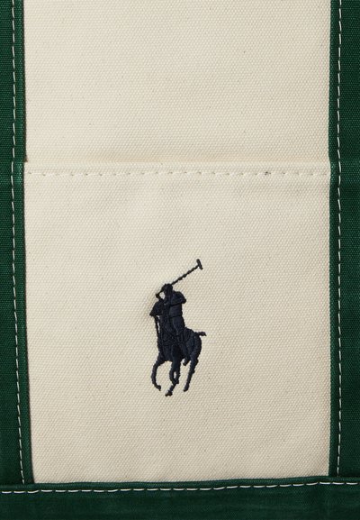 Witte canvasstof met donkergroene gestikte randen en een kleine zwarte geborduurde polo-speler te paard die een geheven knuppel vasthoudt.