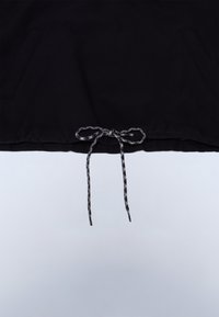 Tela negra con un cordón con estampado en blanco y negro atado en un lazo en el borde inferior central.