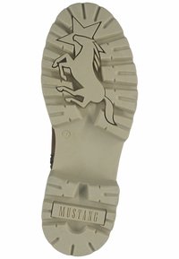 Semelle en caoutchouc avec un motif en relief illustrant un cheval cabré et une étoile. Couleur beige, semelle texturée pour une meilleure adhérence, et "MUSTANG" gravé au fond.
